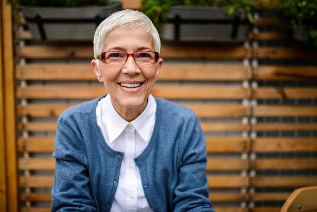 mature woman in glasses smiling in front of a wooden screen