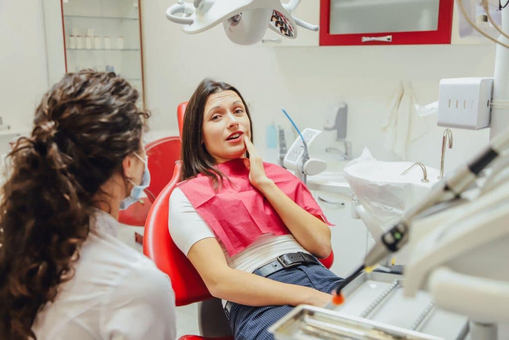 young woman holds jaw while sitting in dental chair