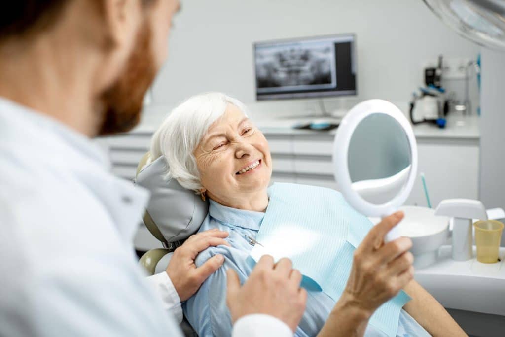 mature woman in dental chair smiles at hand mirror