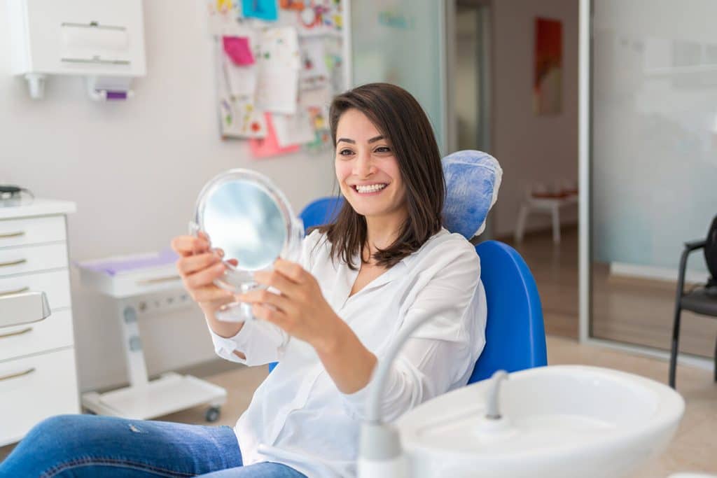 woman in dental chair looks at her teeth in a hand mirror