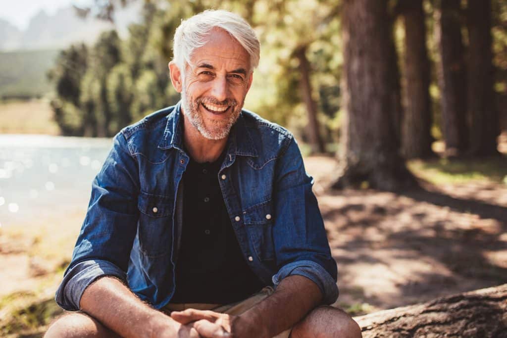 smiling mature man sits by a lake